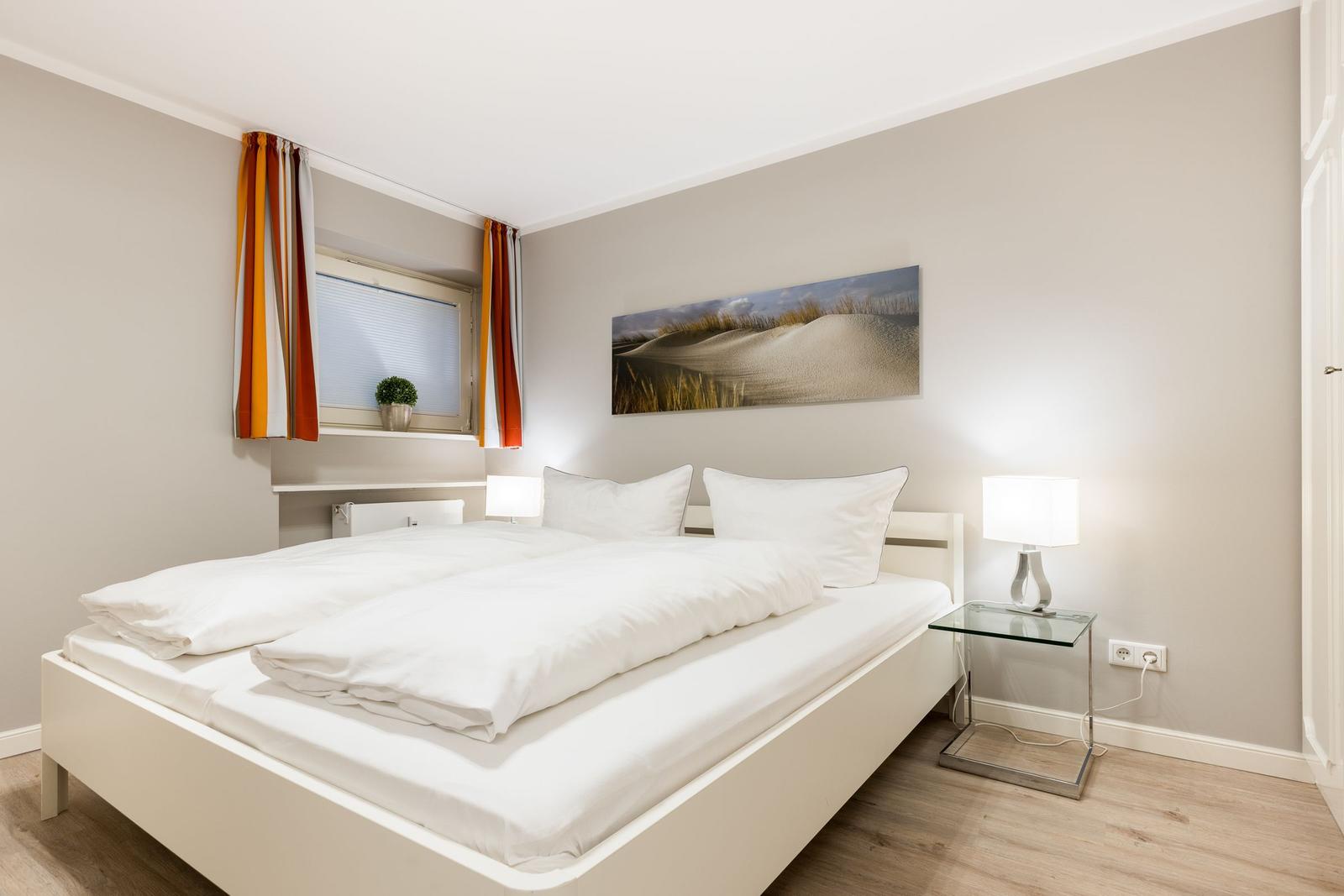 Schlafzimmer mit weißem Bett, Fenster und Wandbild.