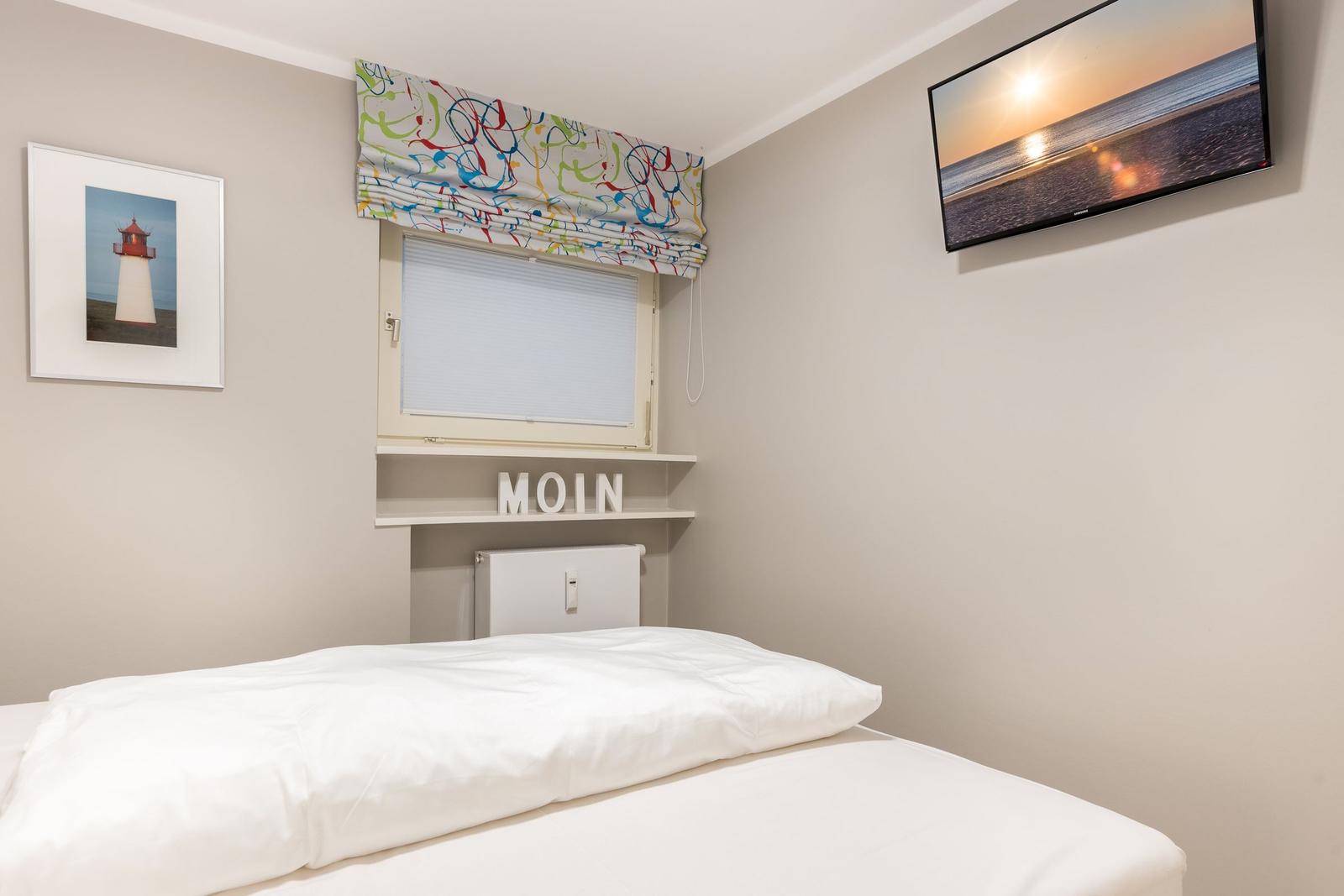 Schlafzimmer mit Bett, TV und Fenster mit Rollladen.