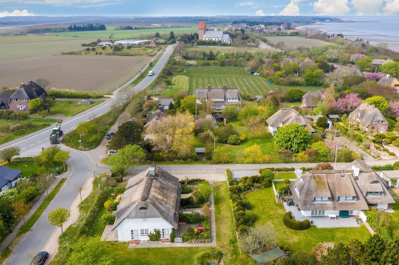 Dorf mit strohgedeckten Häusern und grünen Gärten an der Küste.