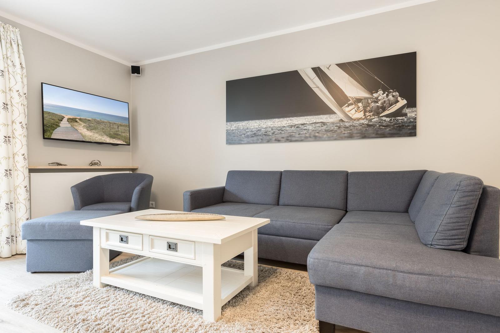 Wohnzimmer mit grauem Sofa, weißem Couchtisch und Wandbild mit Segelboot.