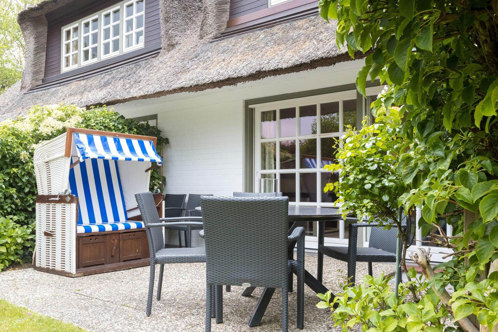 Terrasse mit Gartenmöbeln und Strandkorb vor einem Haus mit Strohdach.