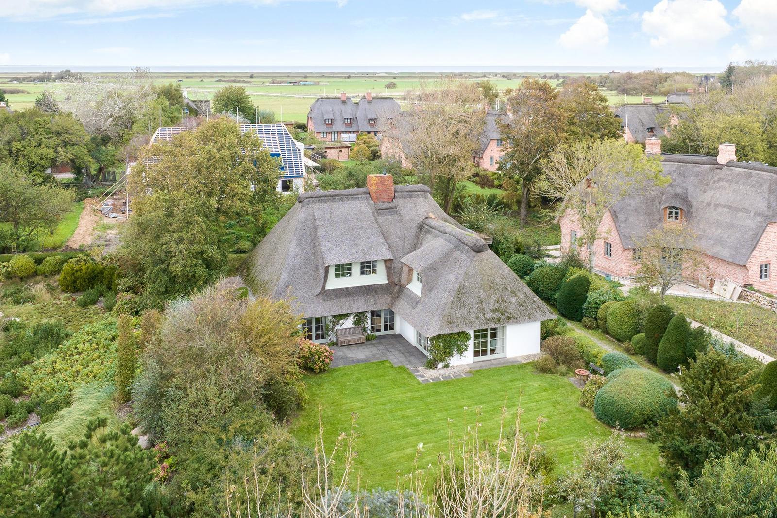 Haus mit Strohdach und Garten. Blick auf Felder und Meer.