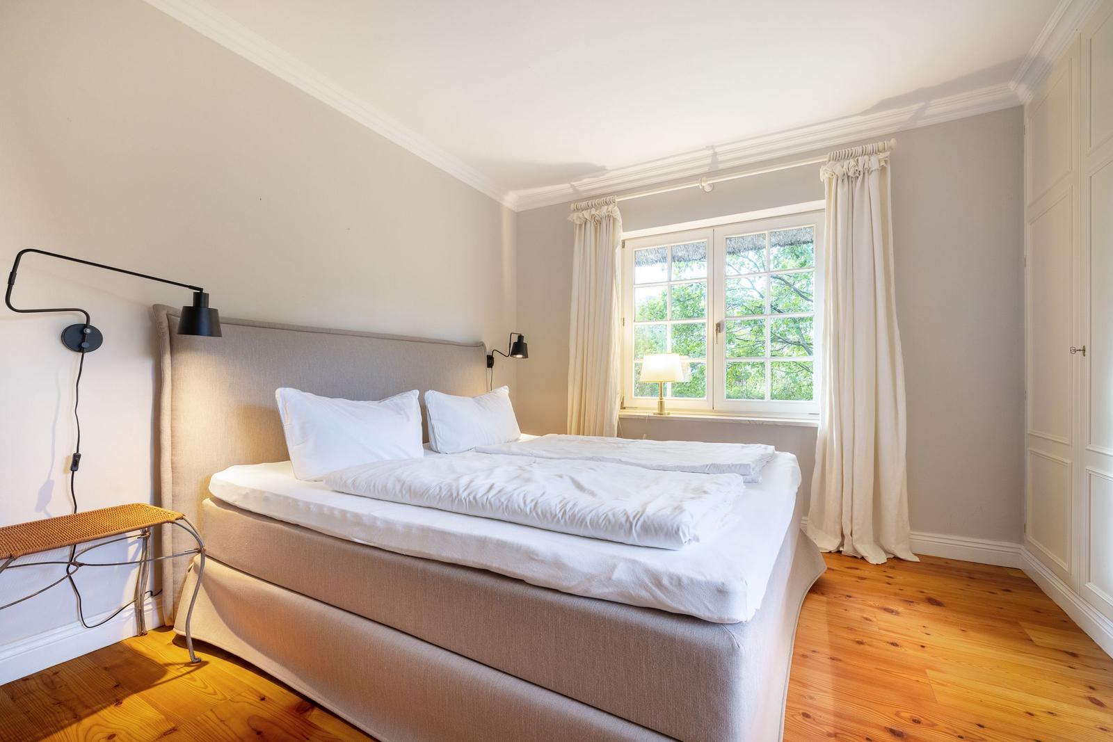 Schlafzimmer mit Bett, Fenster und Holzboden.