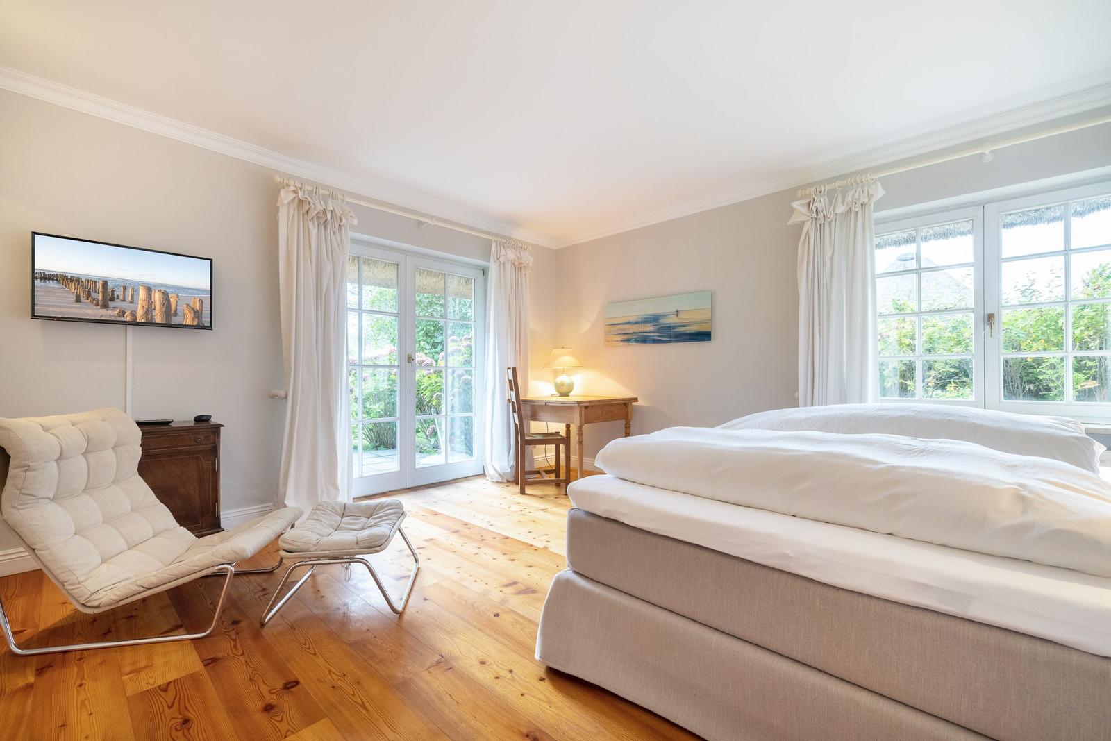 Schlafzimmer mit Bett, TV und Schreibtisch. Holzboden und große Fenster.