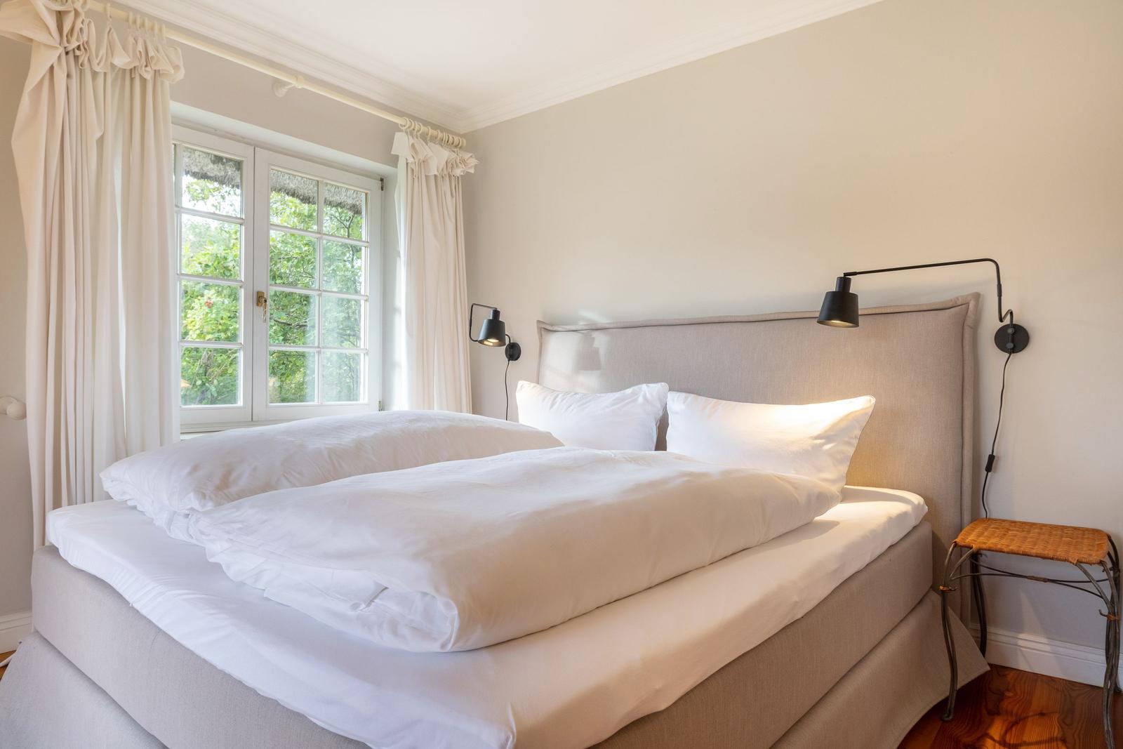 Ein Schlafzimmer mit Doppelbett, Fenster und Wandlampen.