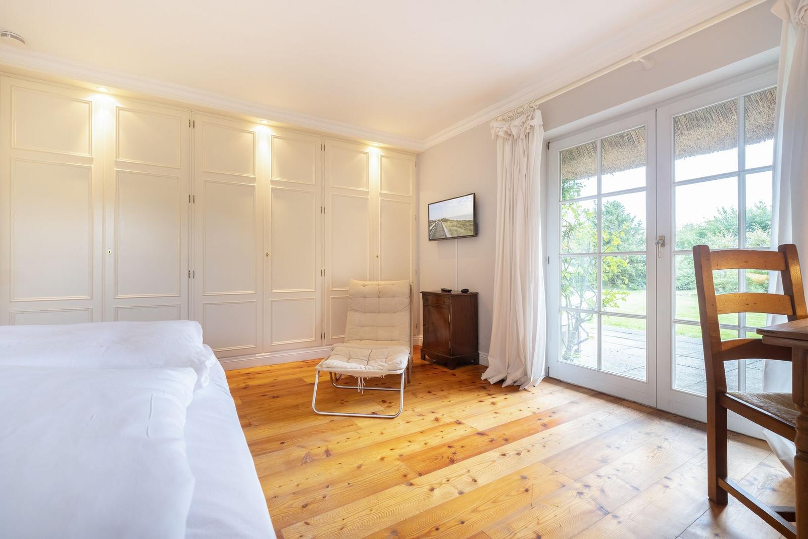 Schlafzimmer mit Holzboden, Bett, Schrank und Glastür zum Garten.
