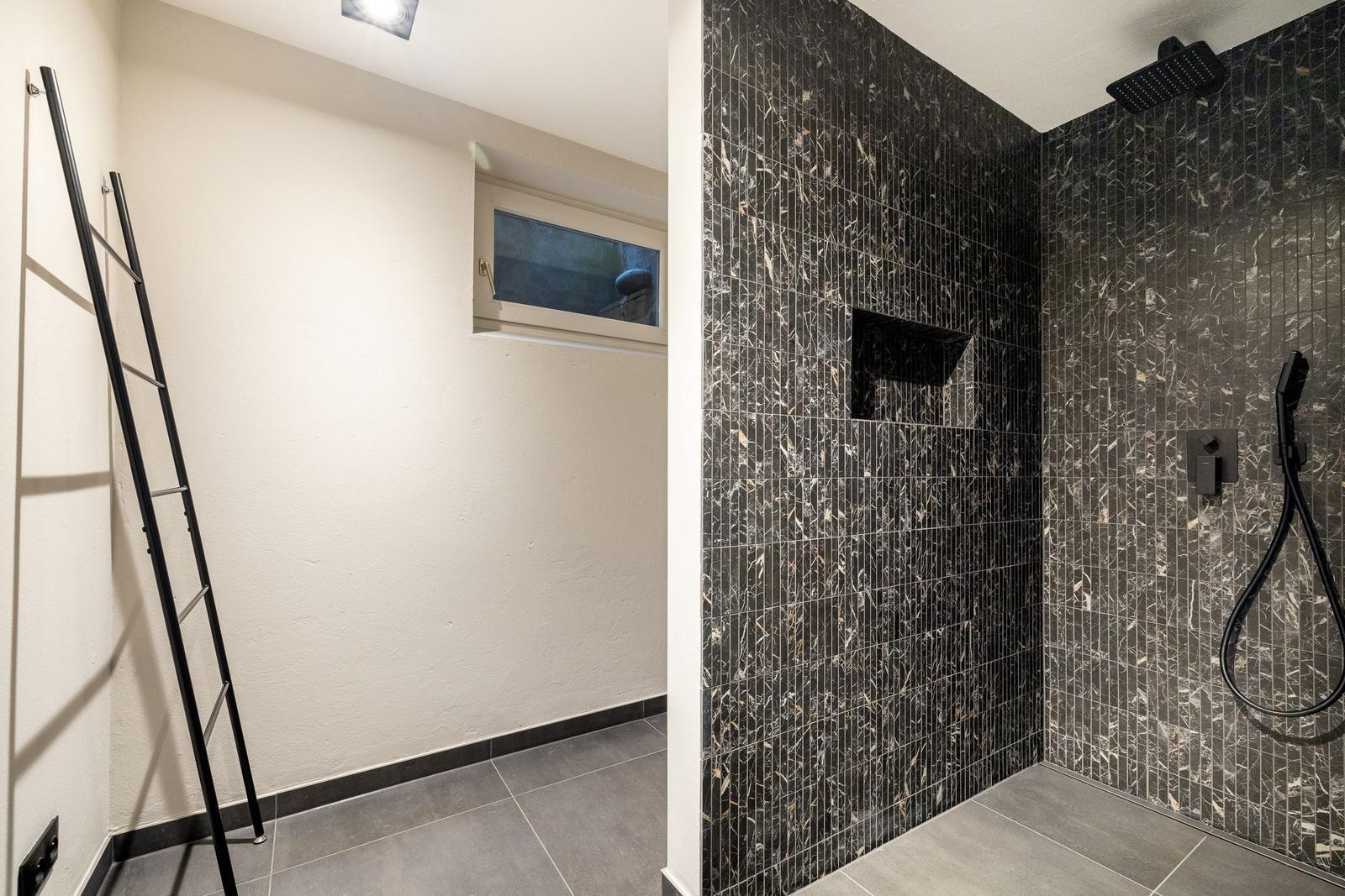 Dusche mit dunklen Mosaikfliesen und Fenster im Bad