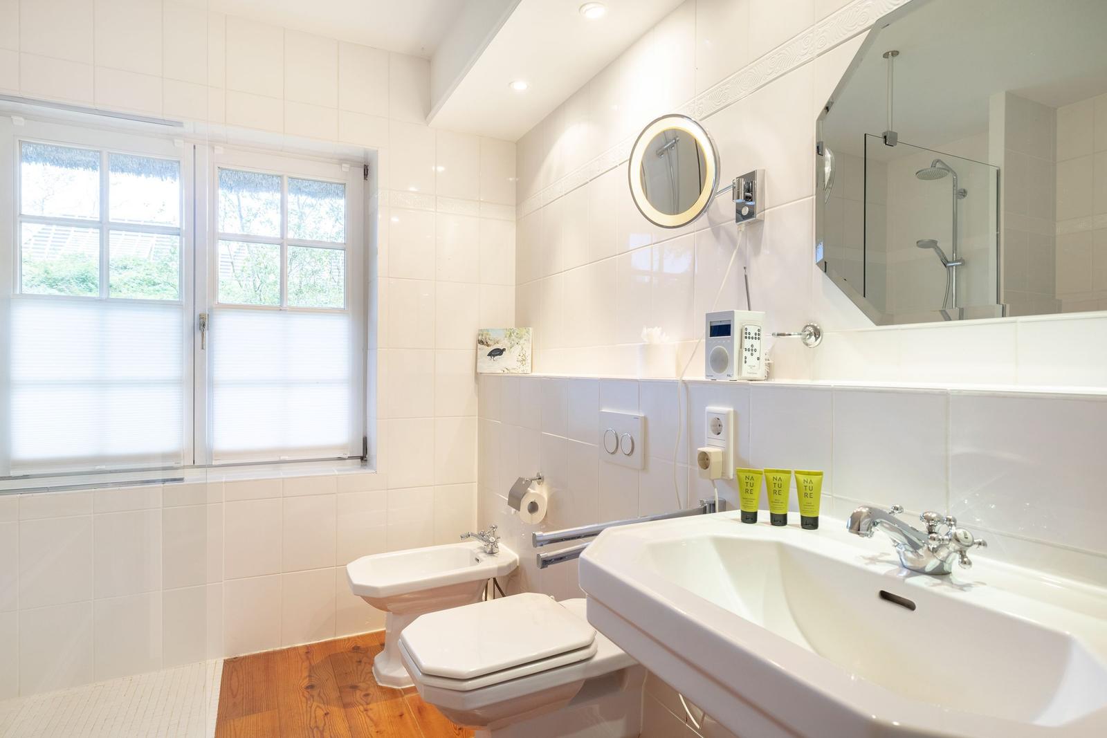 Badezimmer mit Waschbecken, Toilette, Bidet und Dusche. Fenster mit Jalousie. Holzboden.