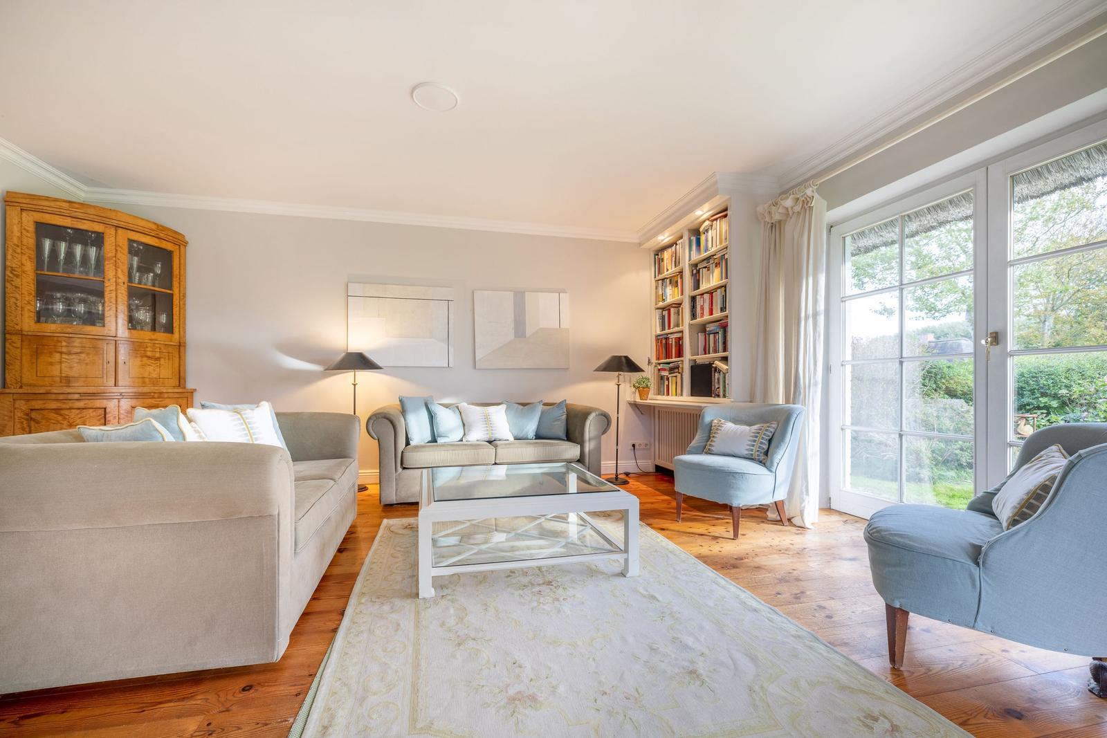 Wohnzimmer mit Sofa, Sessel und Bücherregal. Holzboden und große Fenster.