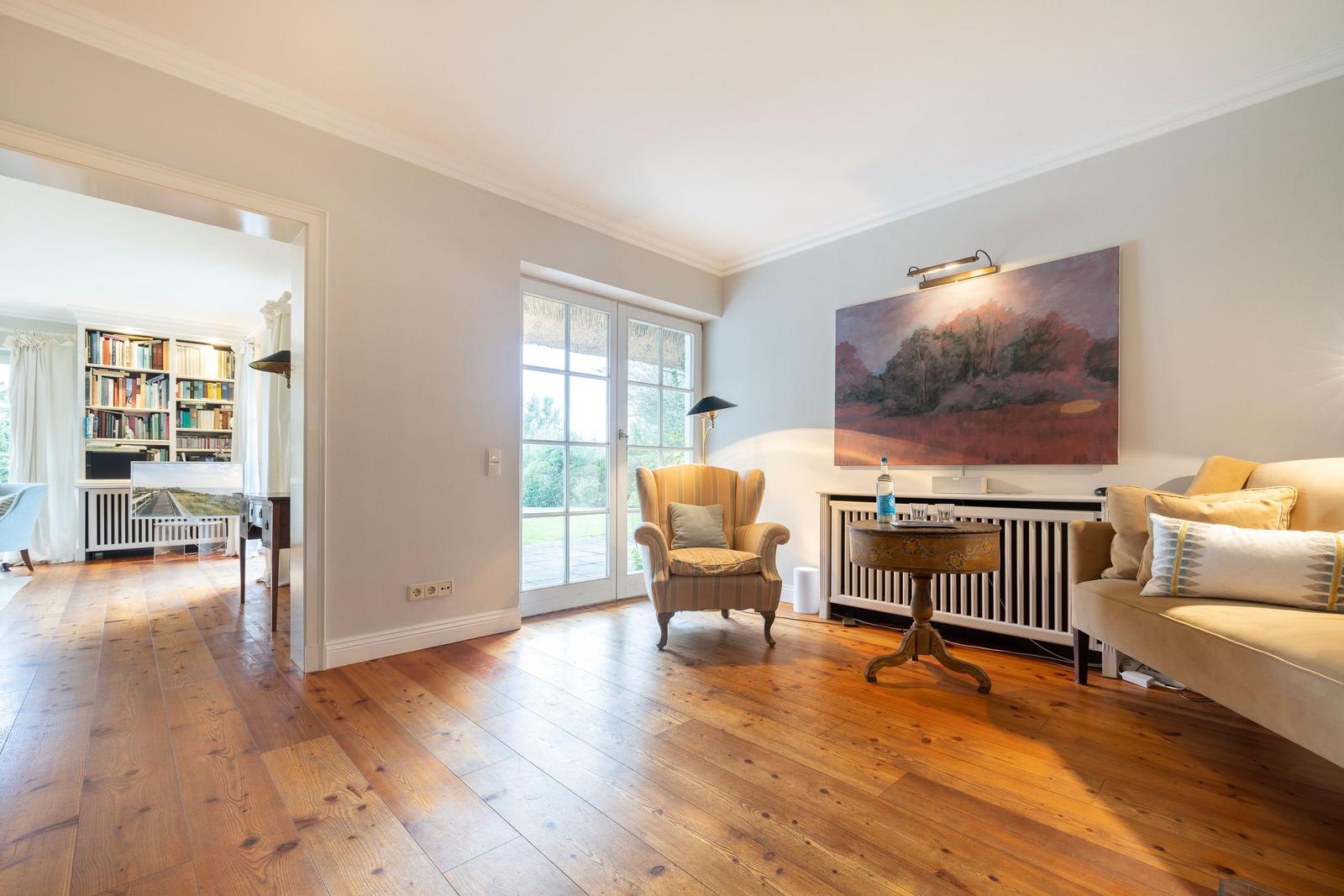 Wohnzimmer mit Holzboden, Sessel, Sofa und Gemälde an der Wand.
