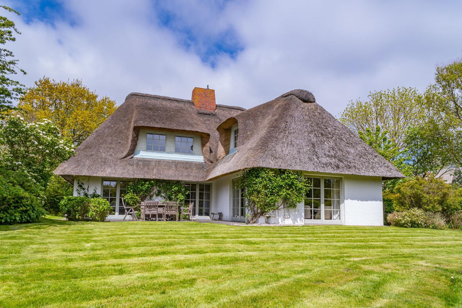 Haus mit Strohdach, weißer Fassade und Garten mit Tisch und Stühlen.