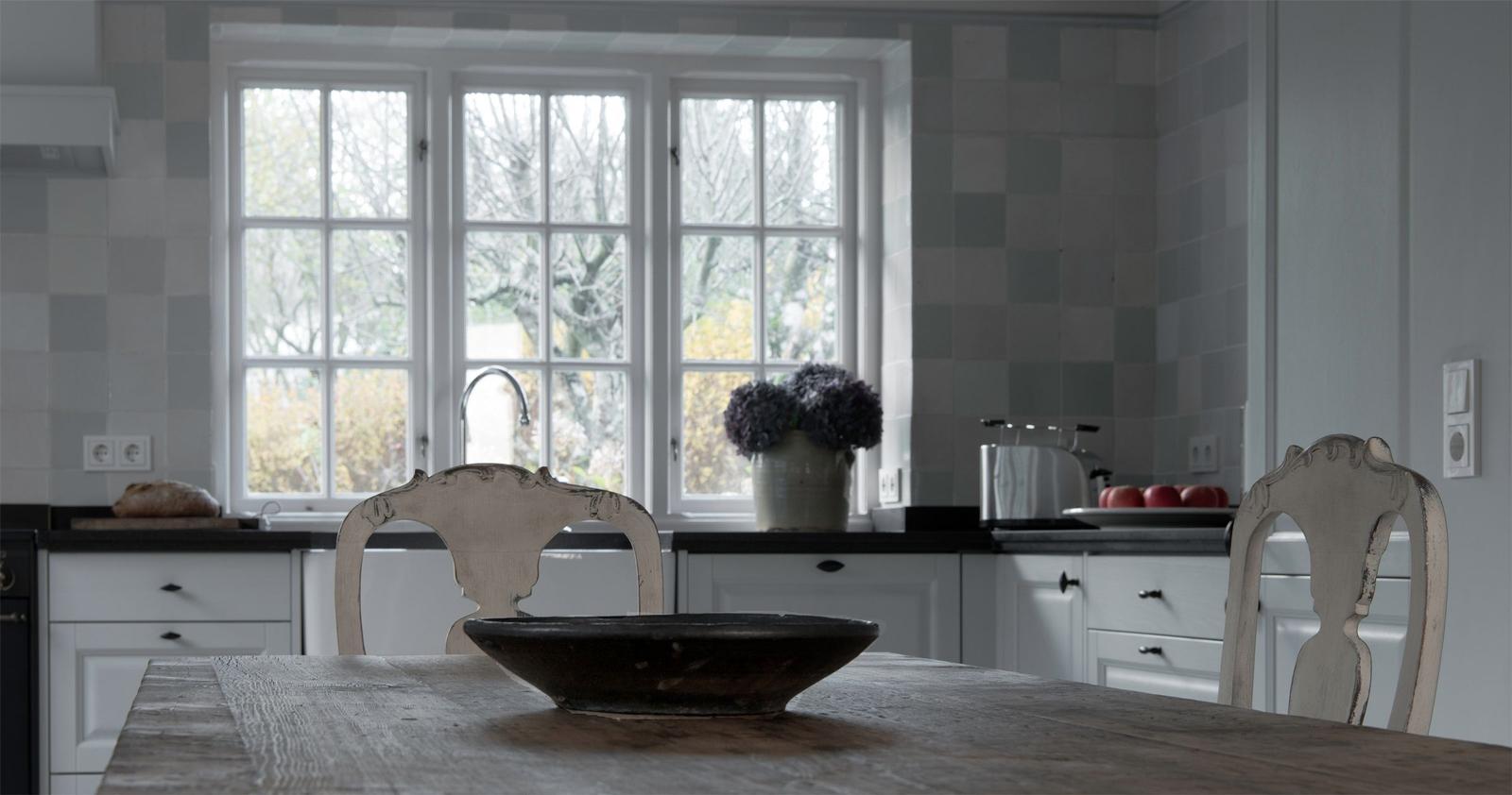 Kitchen with wooden table, two chairs, and view of trees through windows.