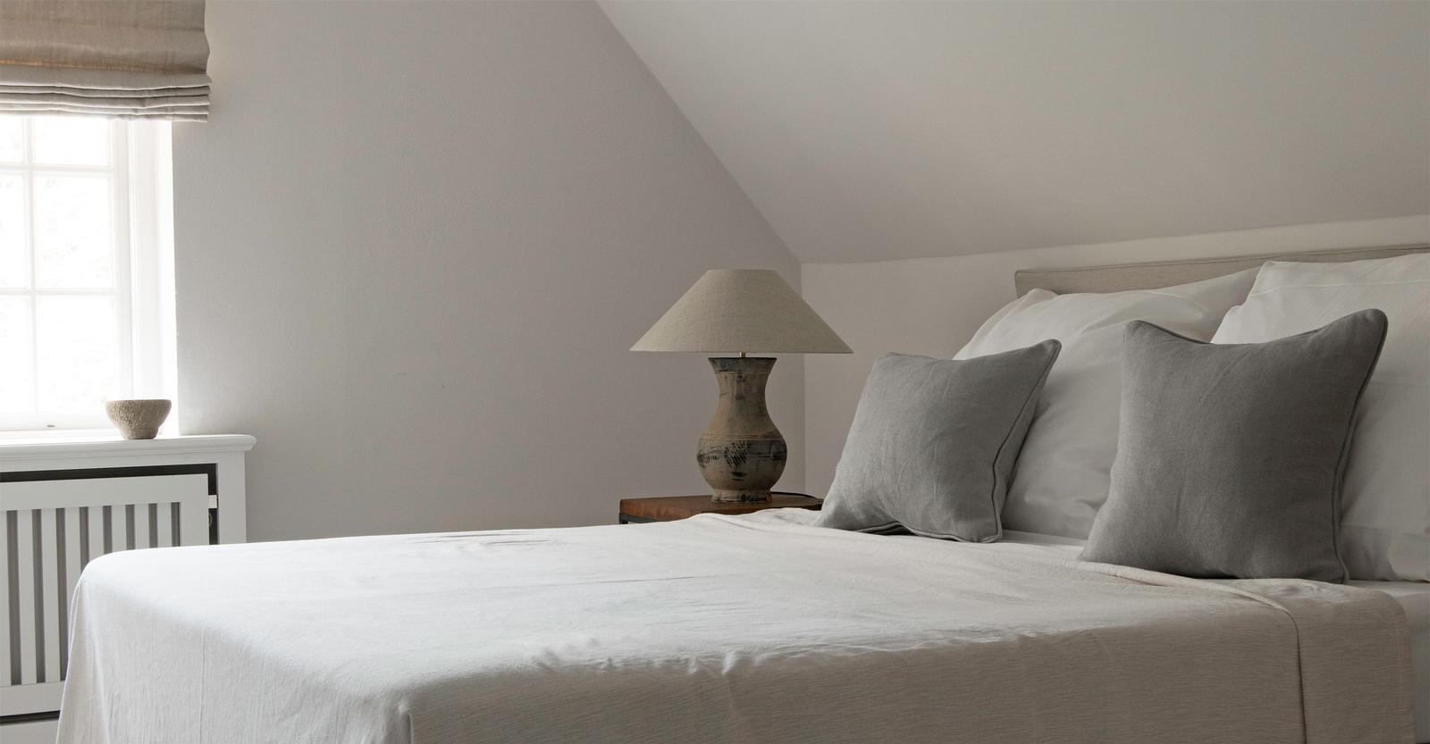 A bedroom with sloped ceiling, bed with pillows and nightstand with lamp.