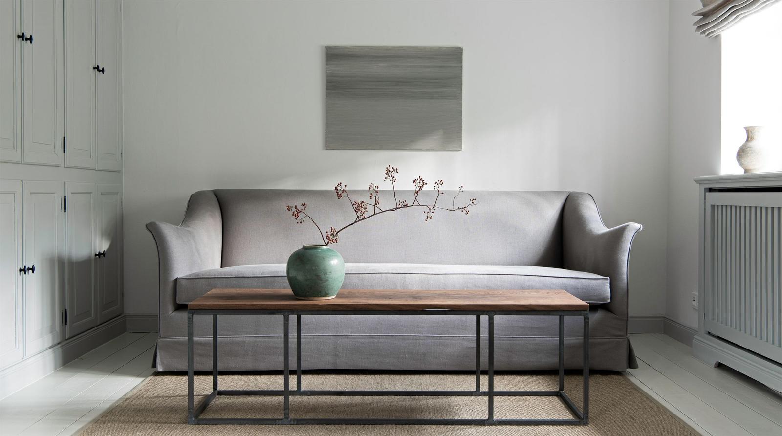 A gray sofa with a wood and metal table in front. A painting hangs behind the sofa.
