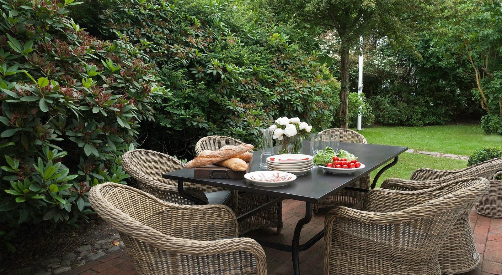 Outdoor dining area with table and chairs, flowers, bread, and vegetables on the table.