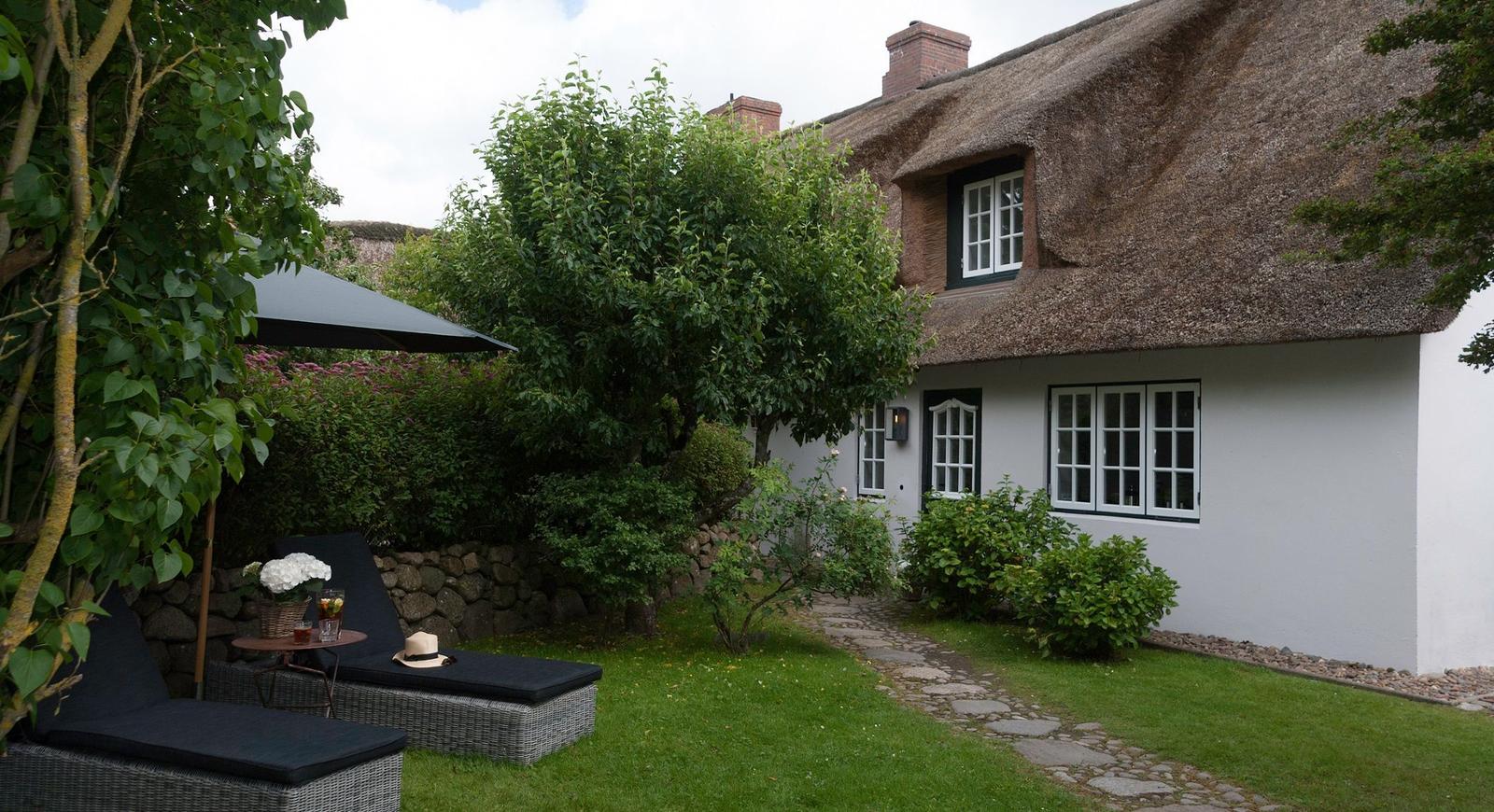 House with thatched roof, garden with loungers and stone path