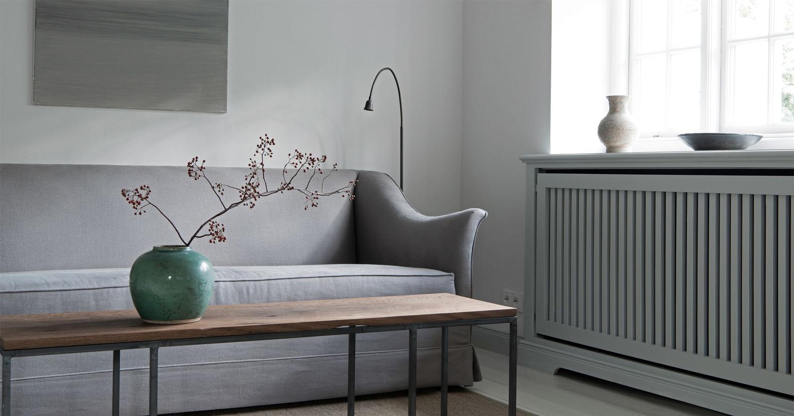 Gray sofa with wooden table and vases. Window and radiator are visible.