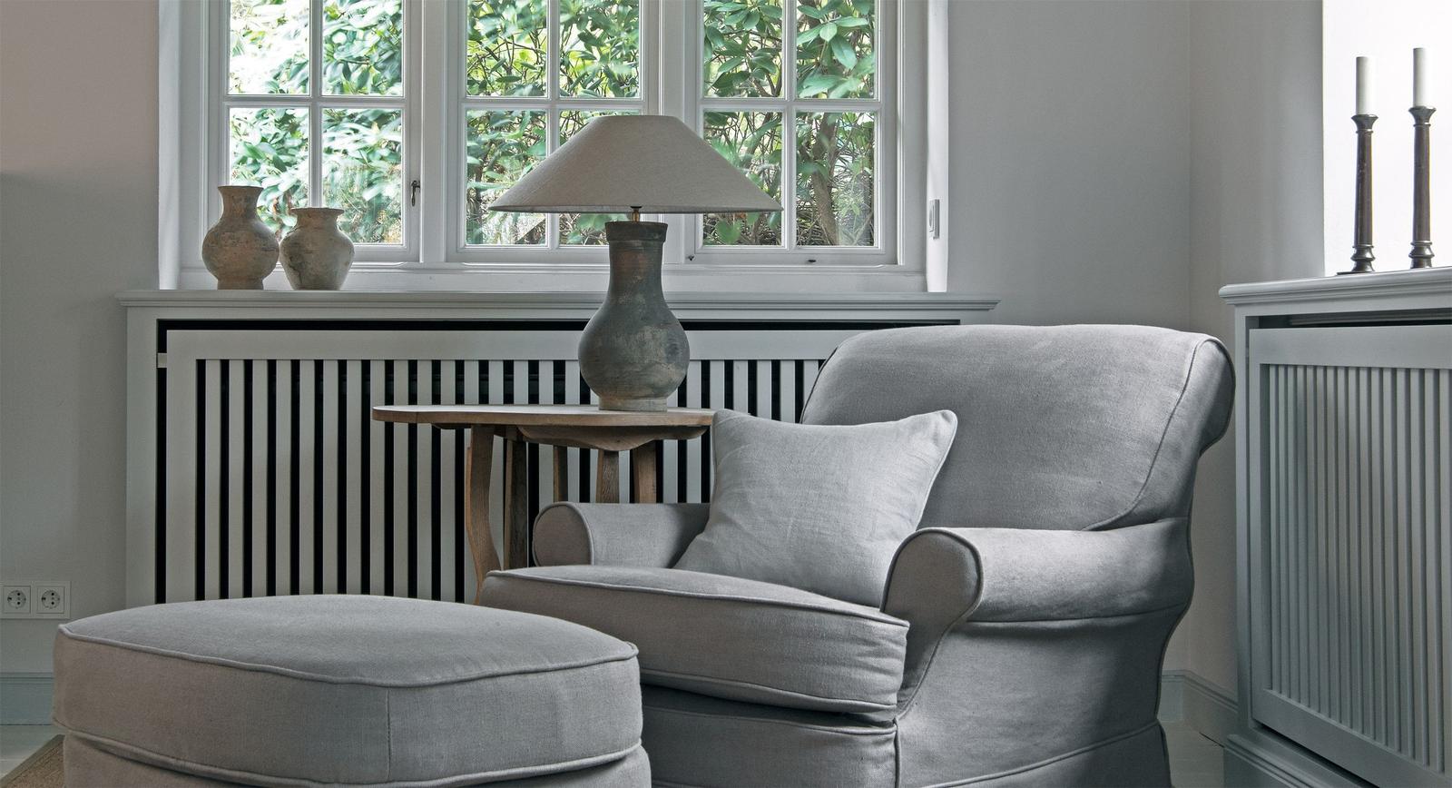 A gray armchair with cushion and ottoman in front of a window with a view of trees.