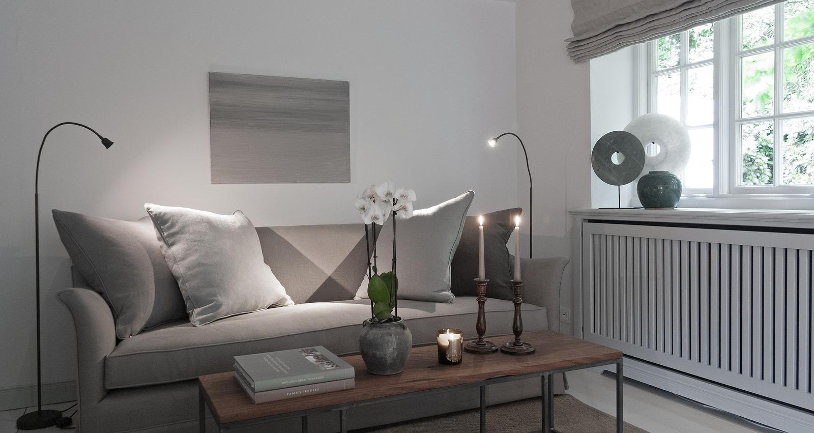 Living room with sofa, table, candles, and flowers. Window with view of greenery.