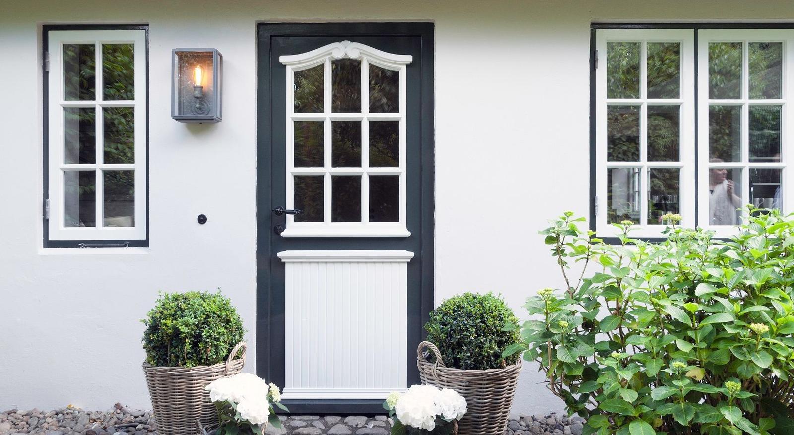 Front door with white windows and potted plants against white wall.