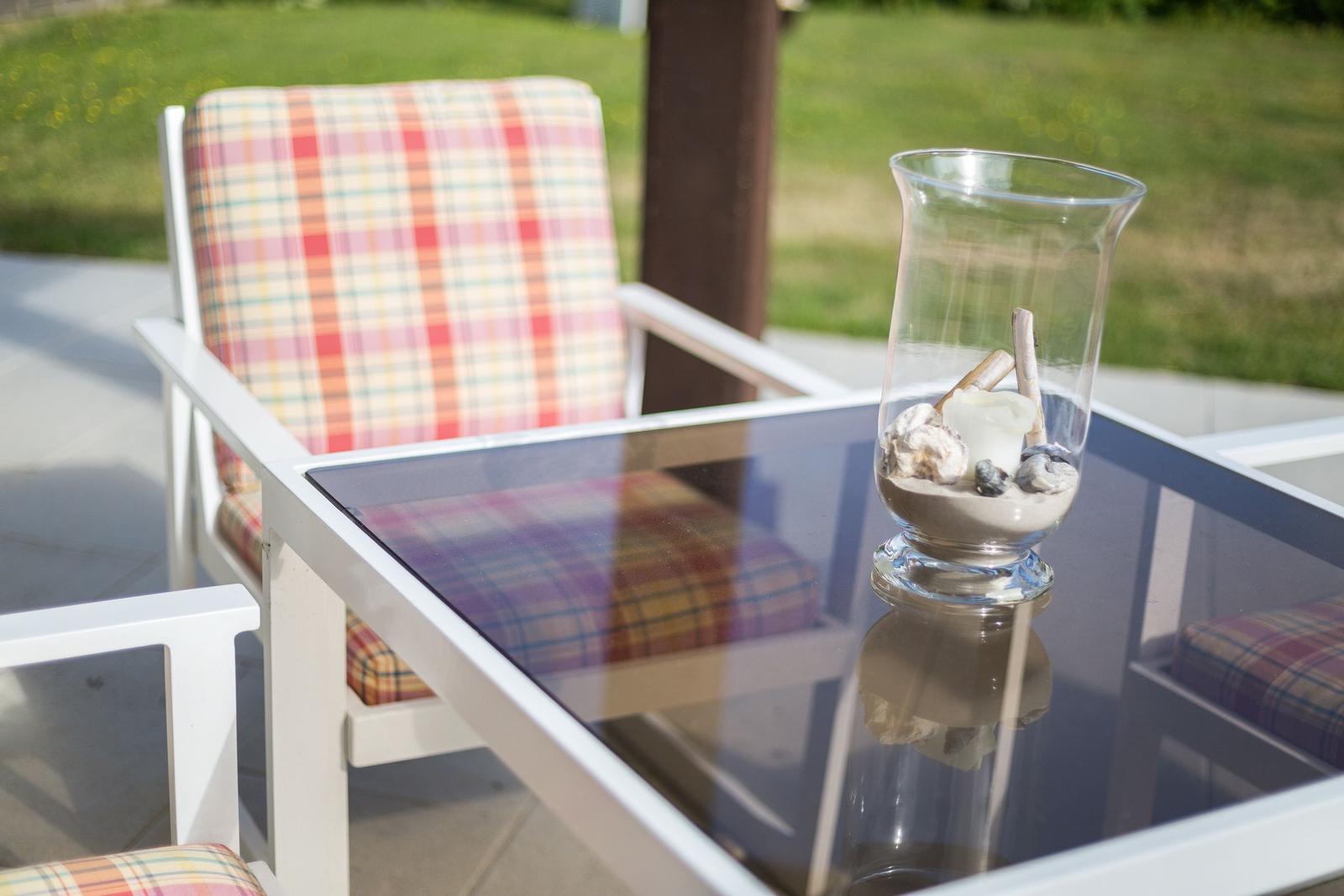 Außenbereich mit Stuhl und Tisch. Auf dem Tisch steht ein Glas mit Steinen und Muscheln.