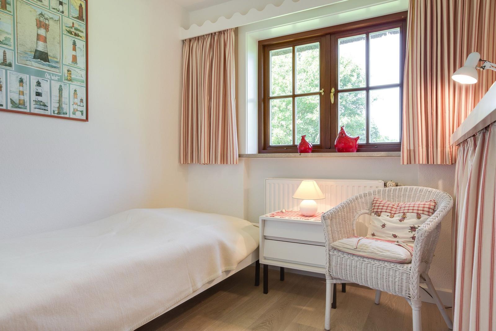 Ein Schlafzimmer mit Bett, Stuhl und Fenster mit Vorhängen.