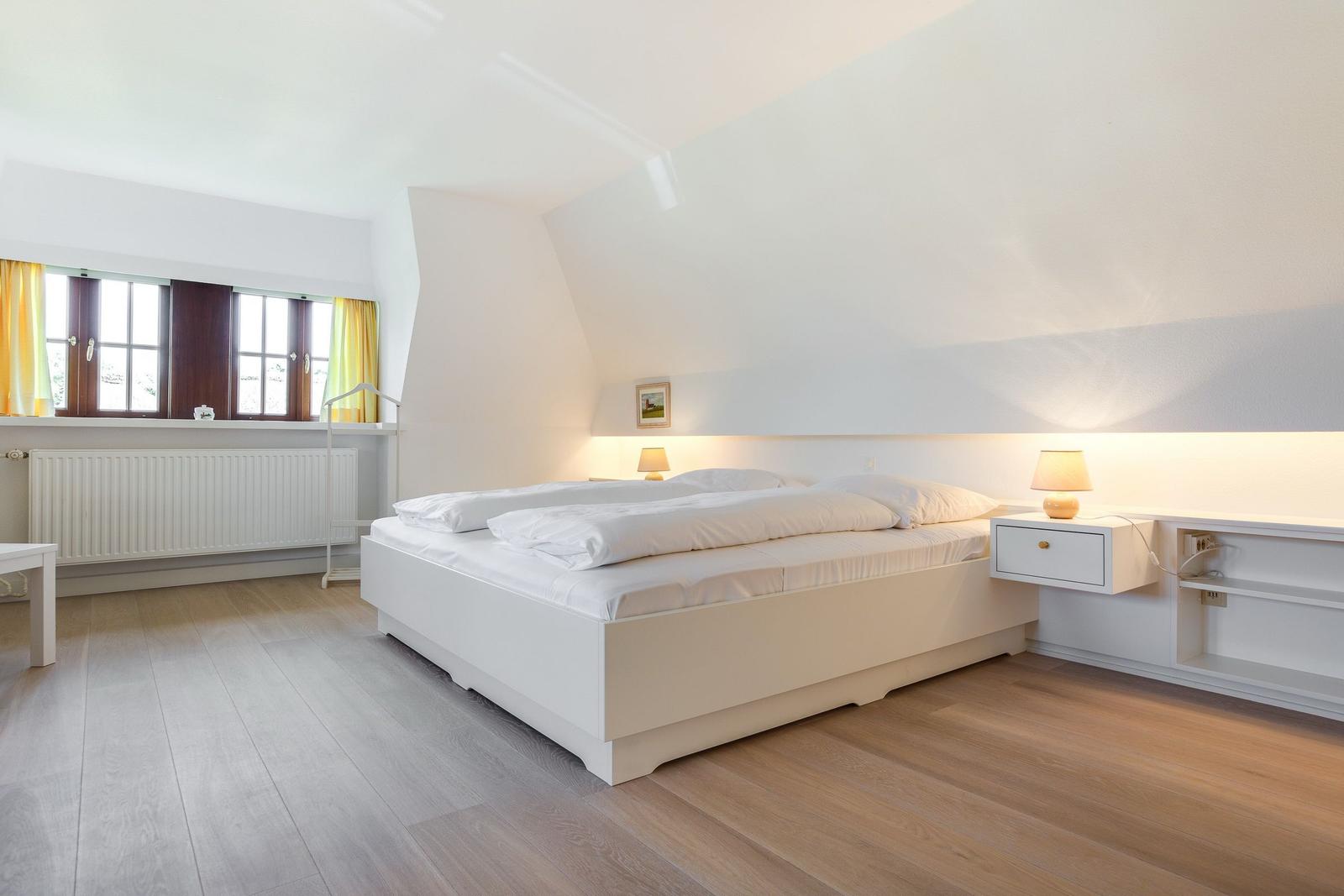 Schlafzimmer mit Doppelbett, Nachttischen und Fenster mit gelben Vorhängen.