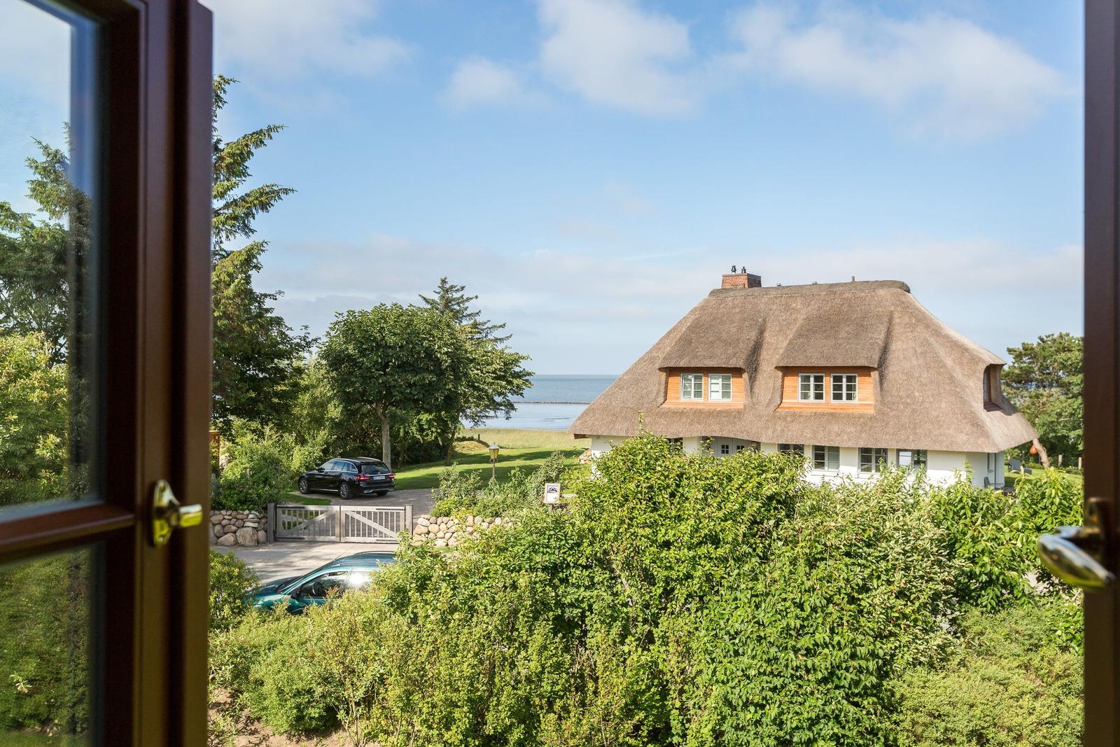 Durch das Fenster ist das Haus mit Strohdach und Blick aufs Meer zu sehen.