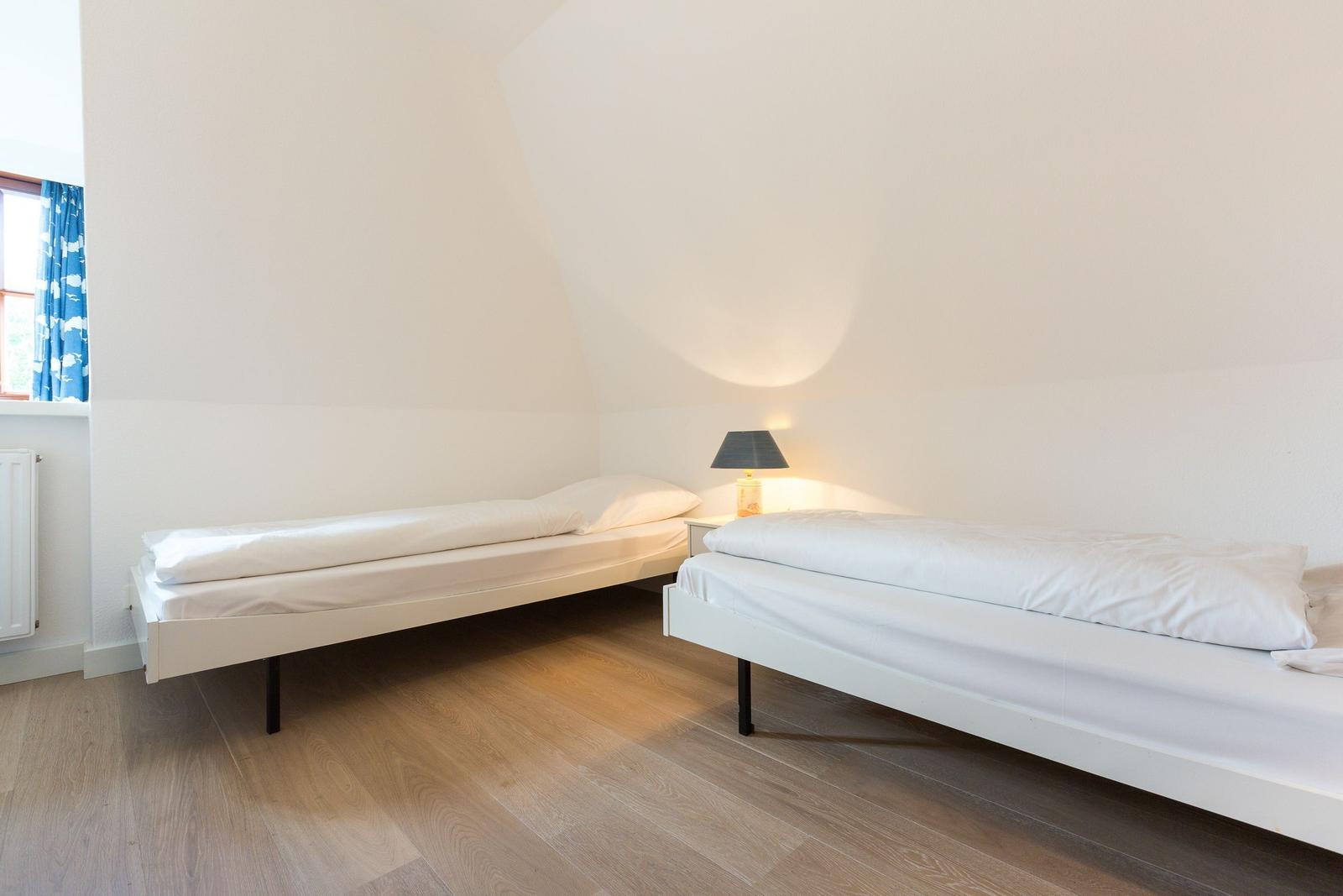 Zwei Betten in einem Raum mit Holzboden und schräger Decke.