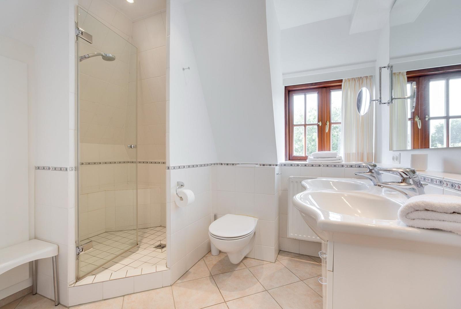Badezimmer mit Dusche, Toilette und Waschbecken. Fenster mit Holzrahmen.