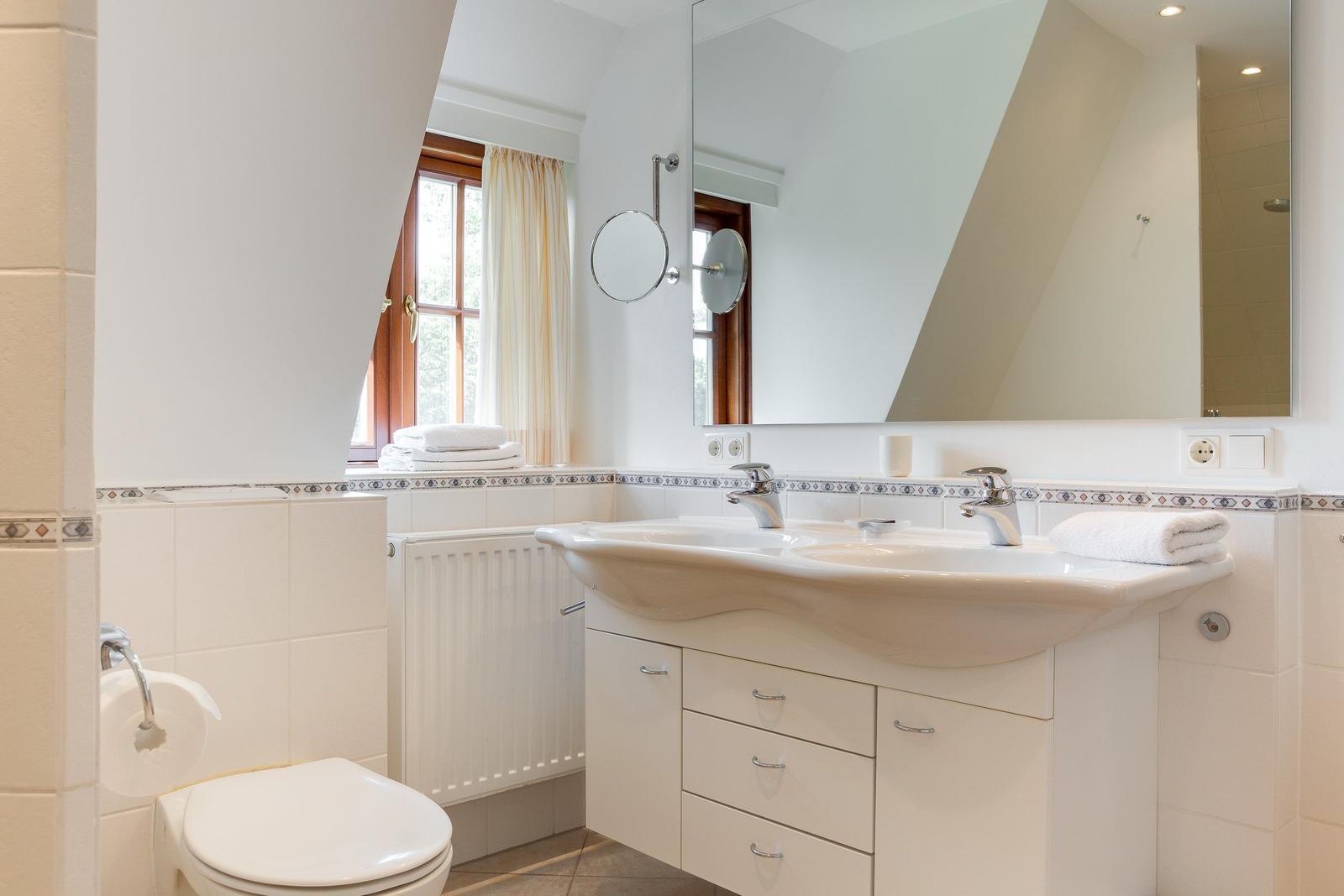 Badezimmer mit Waschbecken, Spiegel, Toilette und Fenster.