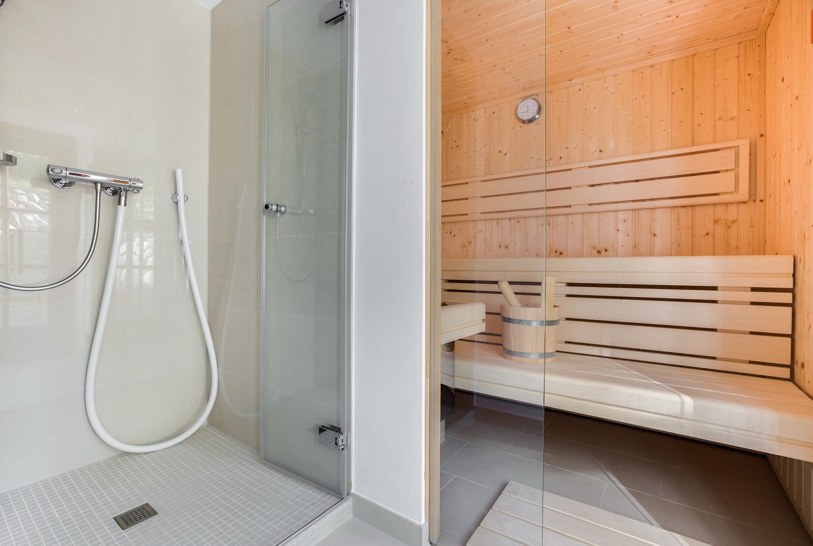 Dusche mit Handbrause und Sauna mit Holzbank und Eimer.