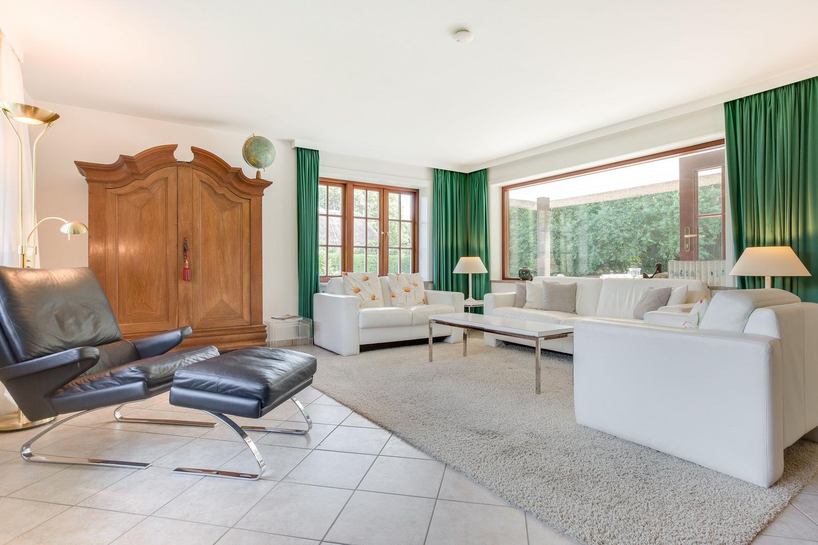 Wohnzimmer mit weißen Sofas, grünen Vorhängen und Holzschrank.