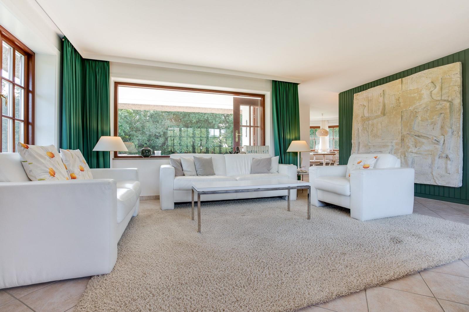Wohnzimmer mit weißen Sofas, grünen Vorhängen und großer Wanddekoration.