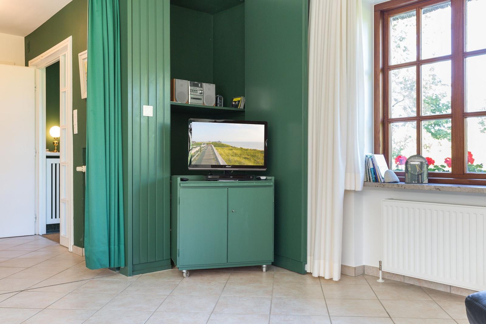 Ein Raum mit grünem Schrank, Fernseher und Fenster mit weißen Vorhängen.