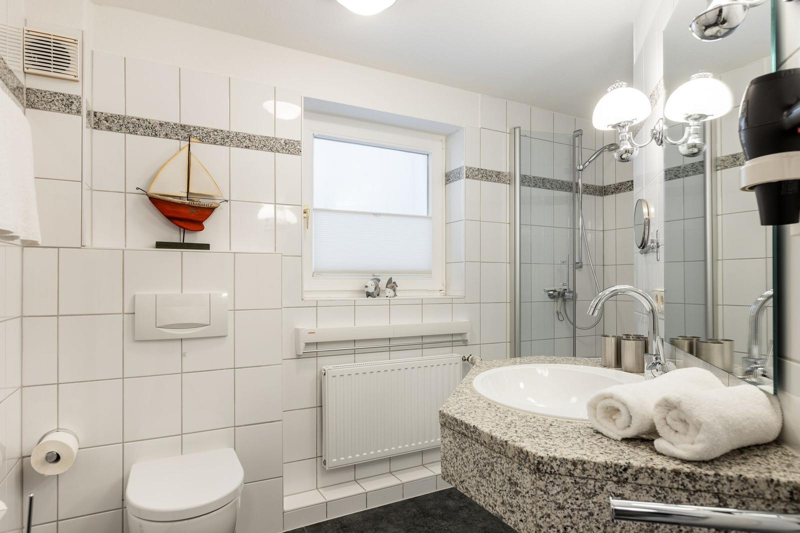 Badezimmer mit Dusche, Waschbecken und Toilette. Wanddekoration mit Segelboot.