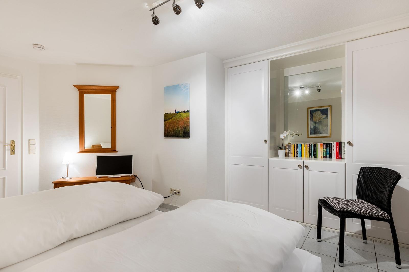 Schlafzimmer mit Bett, Schrank und Stuhl. Wandbild und Spiegel sichtbar.