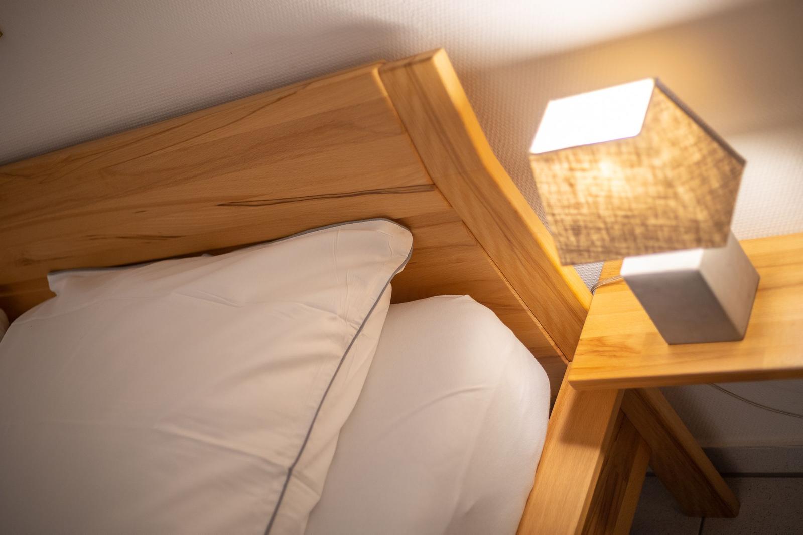 Hölzernes Bett mit weißer Bettwäsche und Nachttisch mit Lampe.