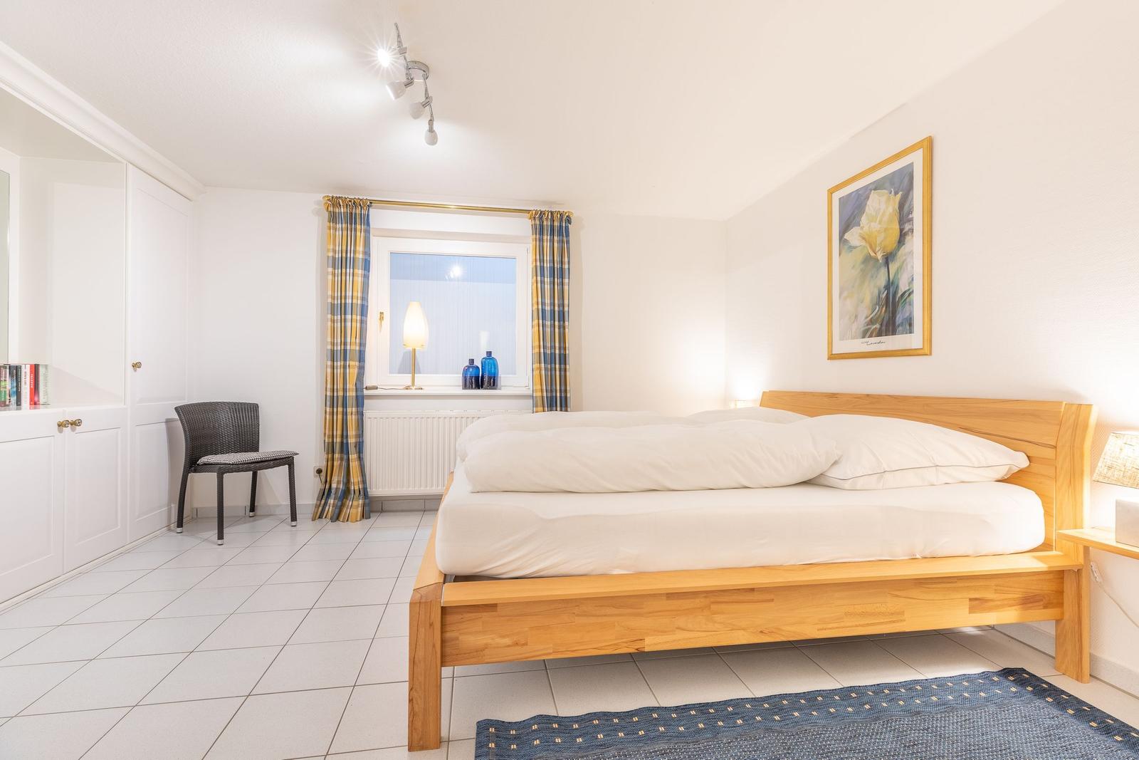 Schlafzimmer mit Holzbett, Fenster mit Vorhängen und Wandbild.