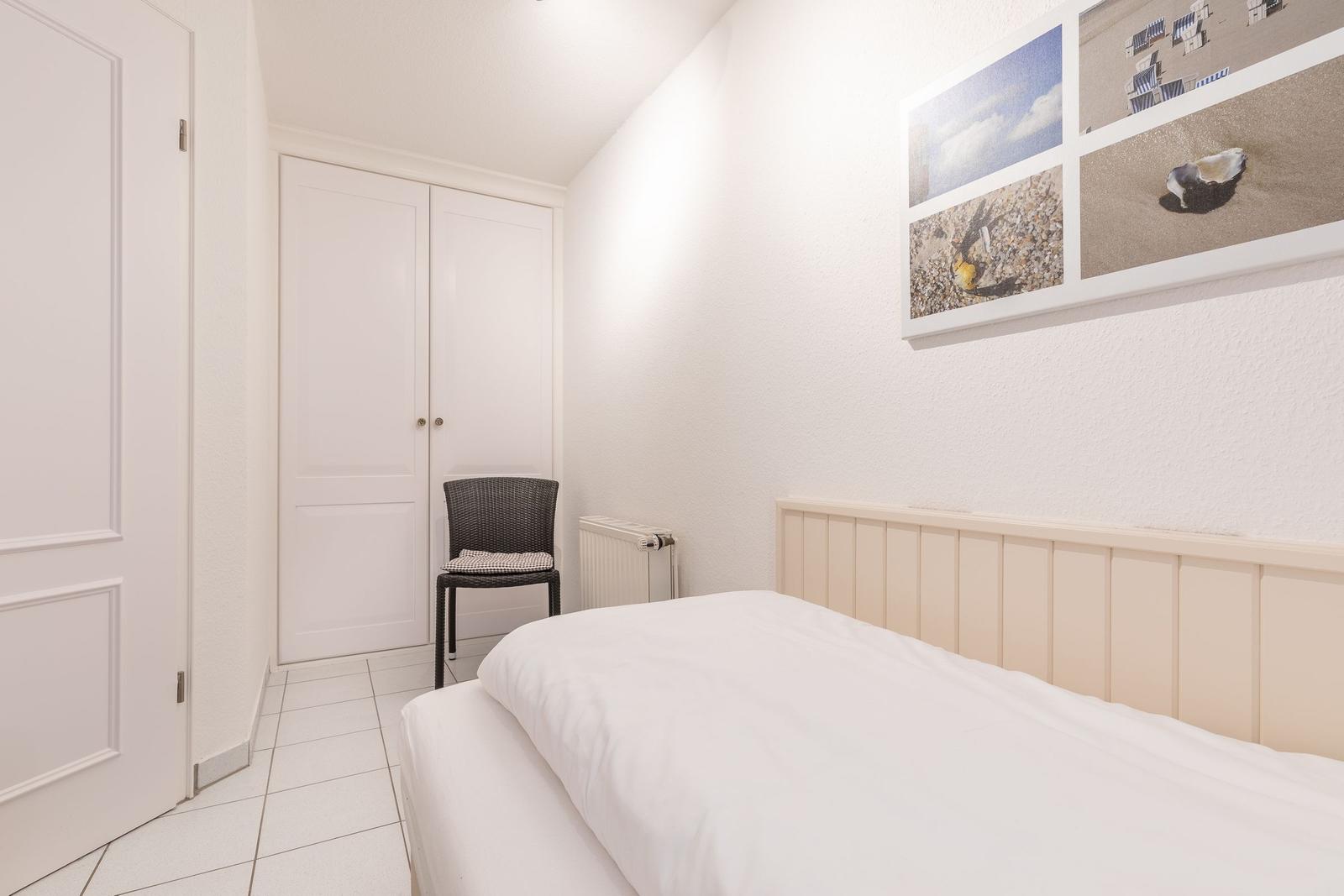 Schlafzimmer mit weißem Bett, Kleiderschrank und Wandbildern.