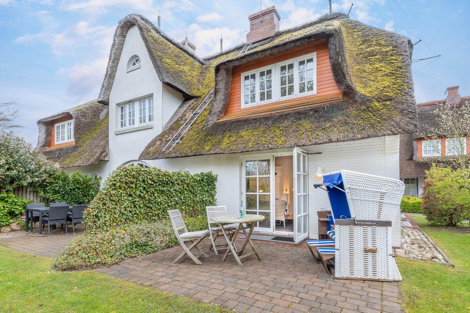 Haus mit strohgedecktem Dach, Terrasse mit Tisch, Stühlen und Strandkorb.