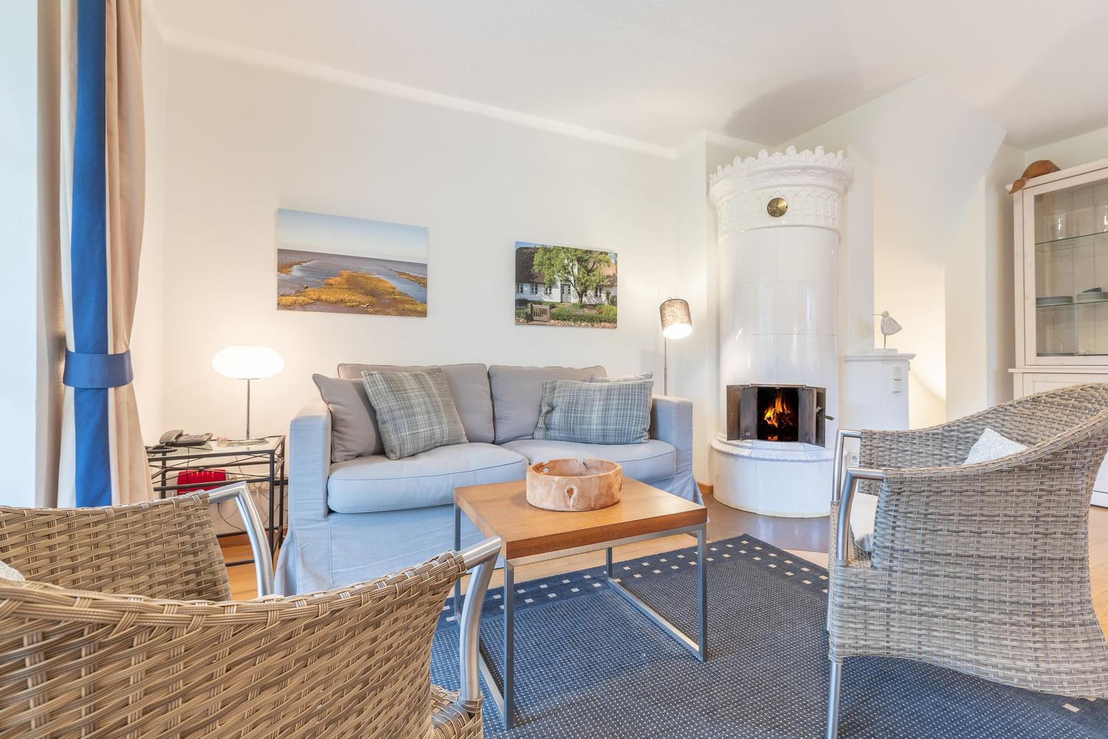Wohnzimmer mit Sofa, Kamin und Stühlen. Wandbilder und Teppich sind sichtbar.