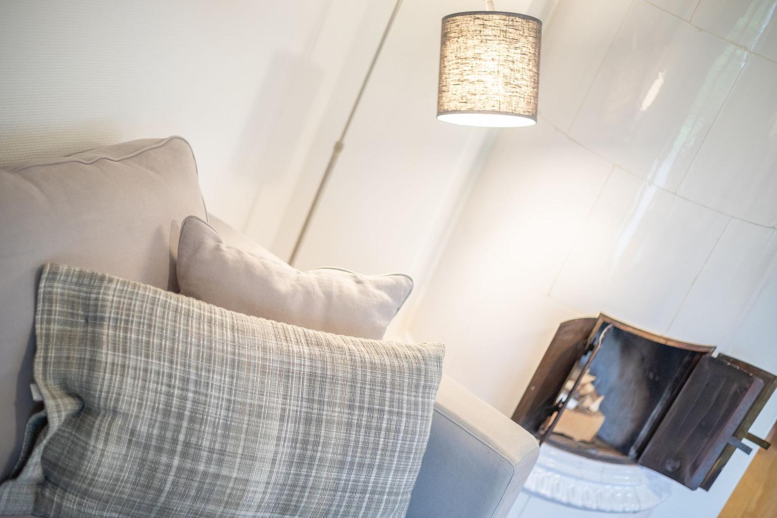 Sofa mit Kissen und Decke, daneben Kamin und Lampe.