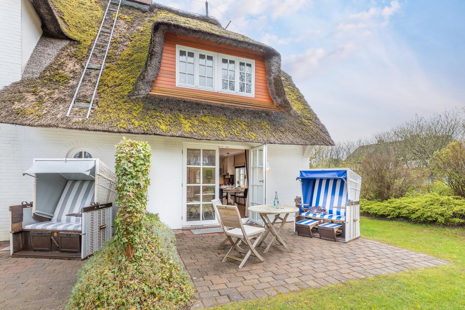 Haus mit strohgedecktem Dach, Terrasse mit Strandkörben und Tisch