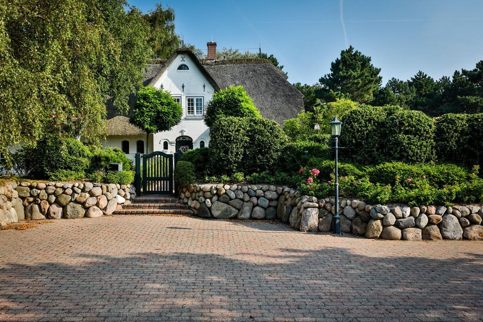 House with thatched roof, stone wall, and paved path.