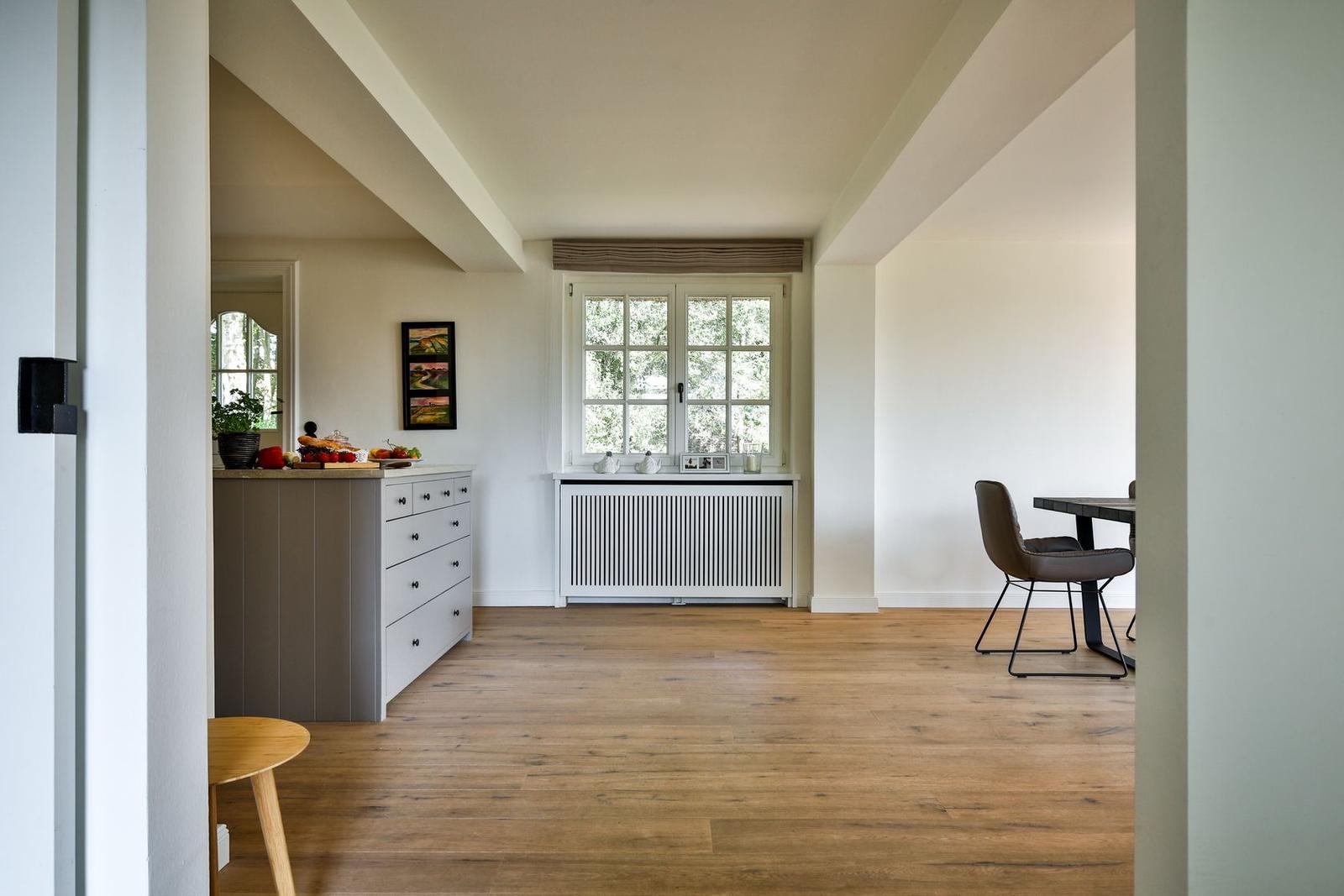 Kitchen with wooden floor, window, and dining area with chair.