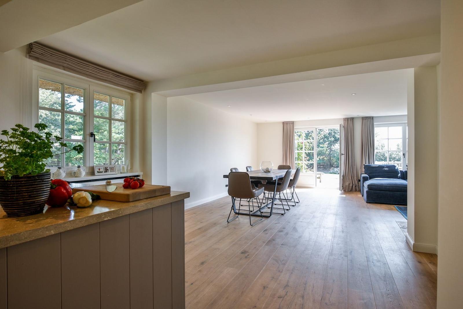 Kitchen with dining area and living room with wooden floor and windows.