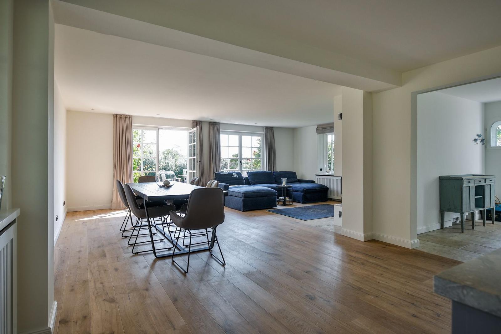 Large living and dining area with wooden floor and blue sofa.