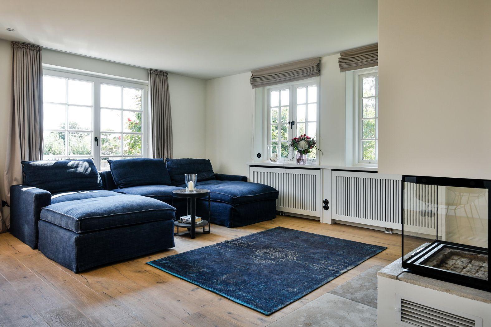 A living room with blue sofa, wooden floor, and windows with curtains.