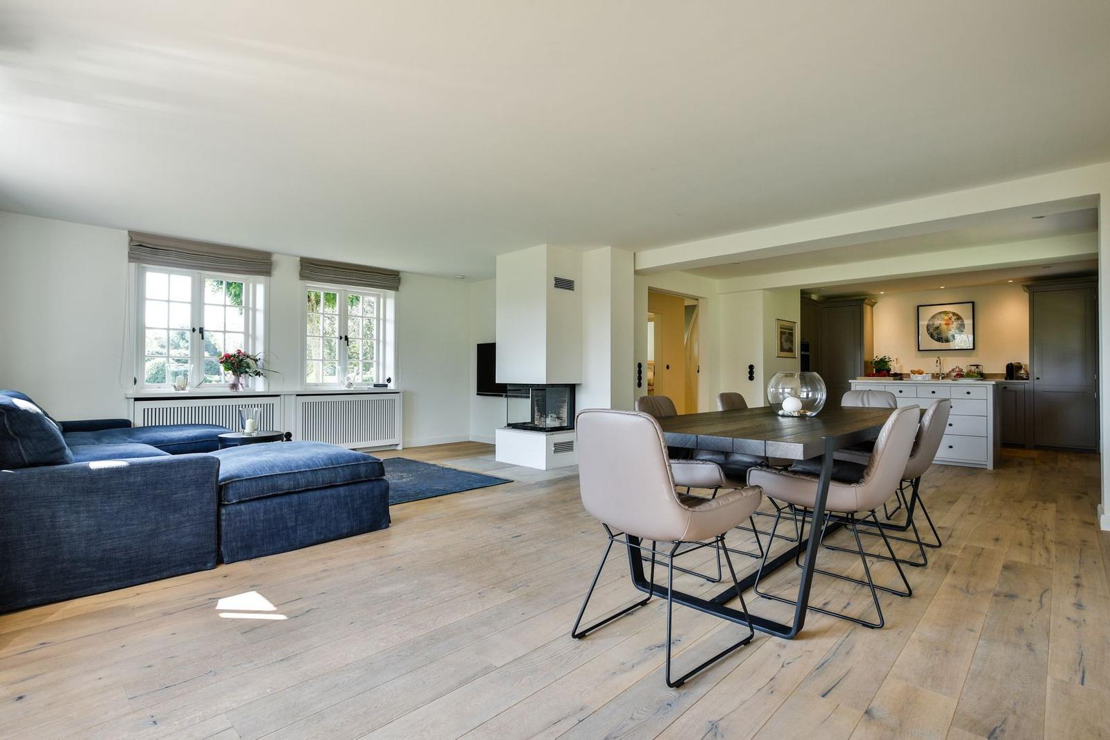 Living and dining area with wooden floor, sofa, dining table, and fireplace.